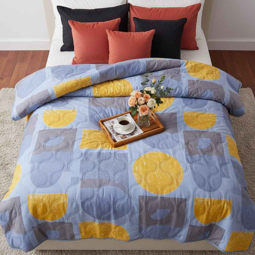 Colorful geometric patterned comforter on a bed with pillows and a tray of coffee and flowers.